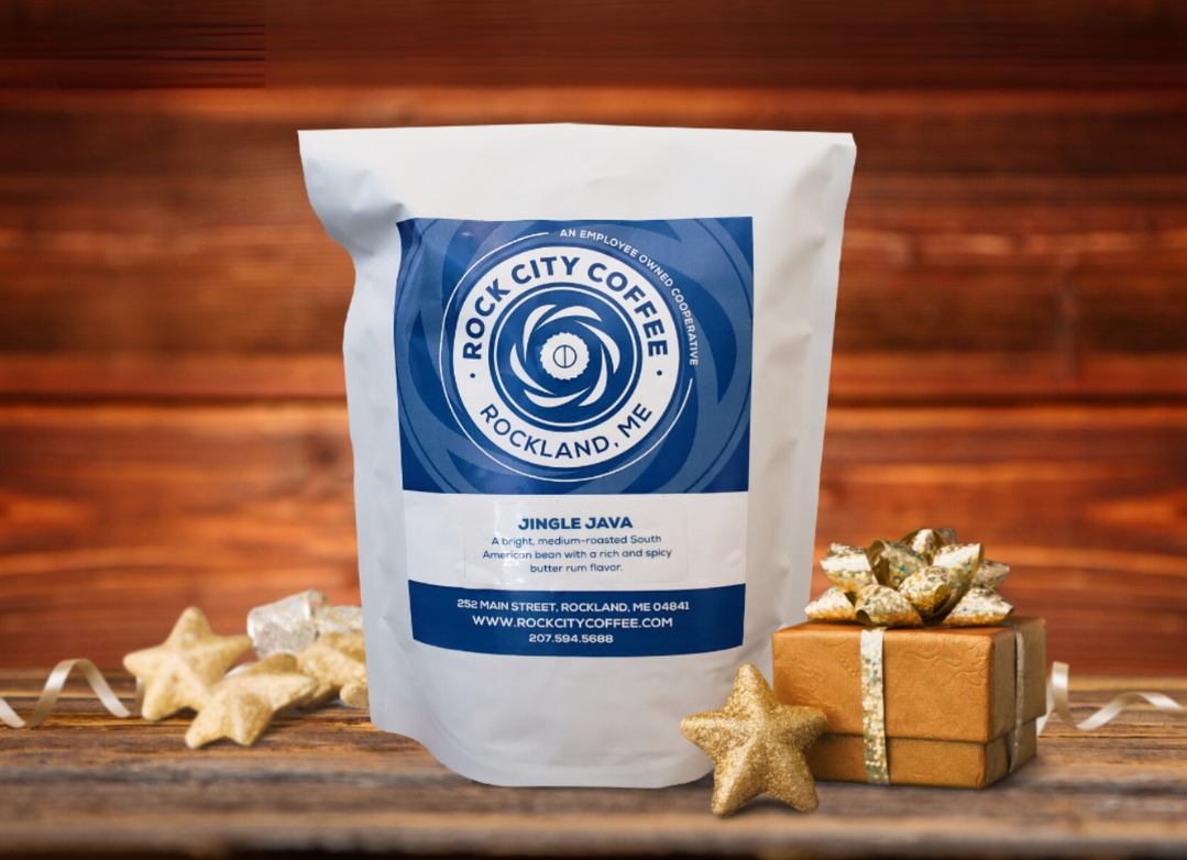 A bag of Jingle Java coffee with a label that reads "A bright, medium-roasted South American bean with a rich and spicy butter rum flavor", sitting amongst golden holiday decorations